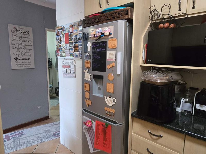 A functional kitchen area featuring laminate cabinetry, granite countertops, and a built-in microwave, with tiled flooring and direct access to an adjacent hallway.