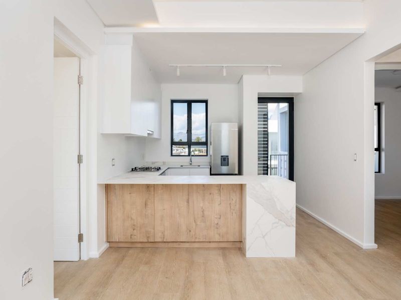 Modern kitchen featuring light wood cabinetry, stone countertops, integrated gas hob, and sleek track lighting in an open-plan layout.