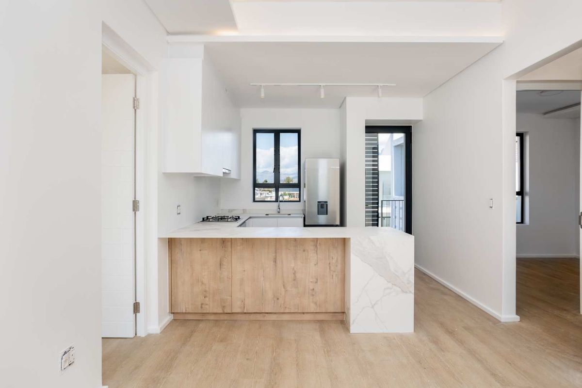 Modern kitchen featuring light wood cabinetry, stone countertops, integrated gas hob, and sleek track lighting in an open-plan layout.