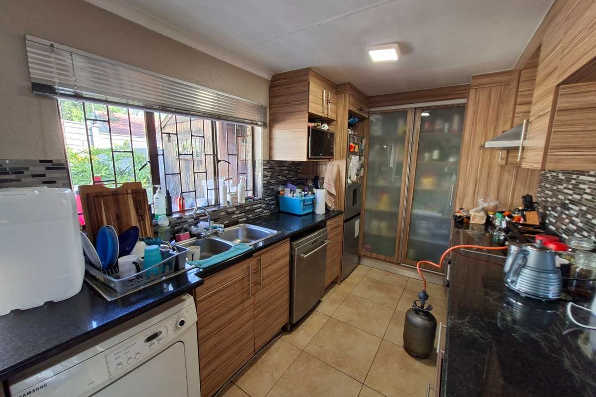 Functional kitchen featuring laminate cabinetry, granite countertops, mosaic tile backsplash, and integrated appliances with tiled flooring and natural light.