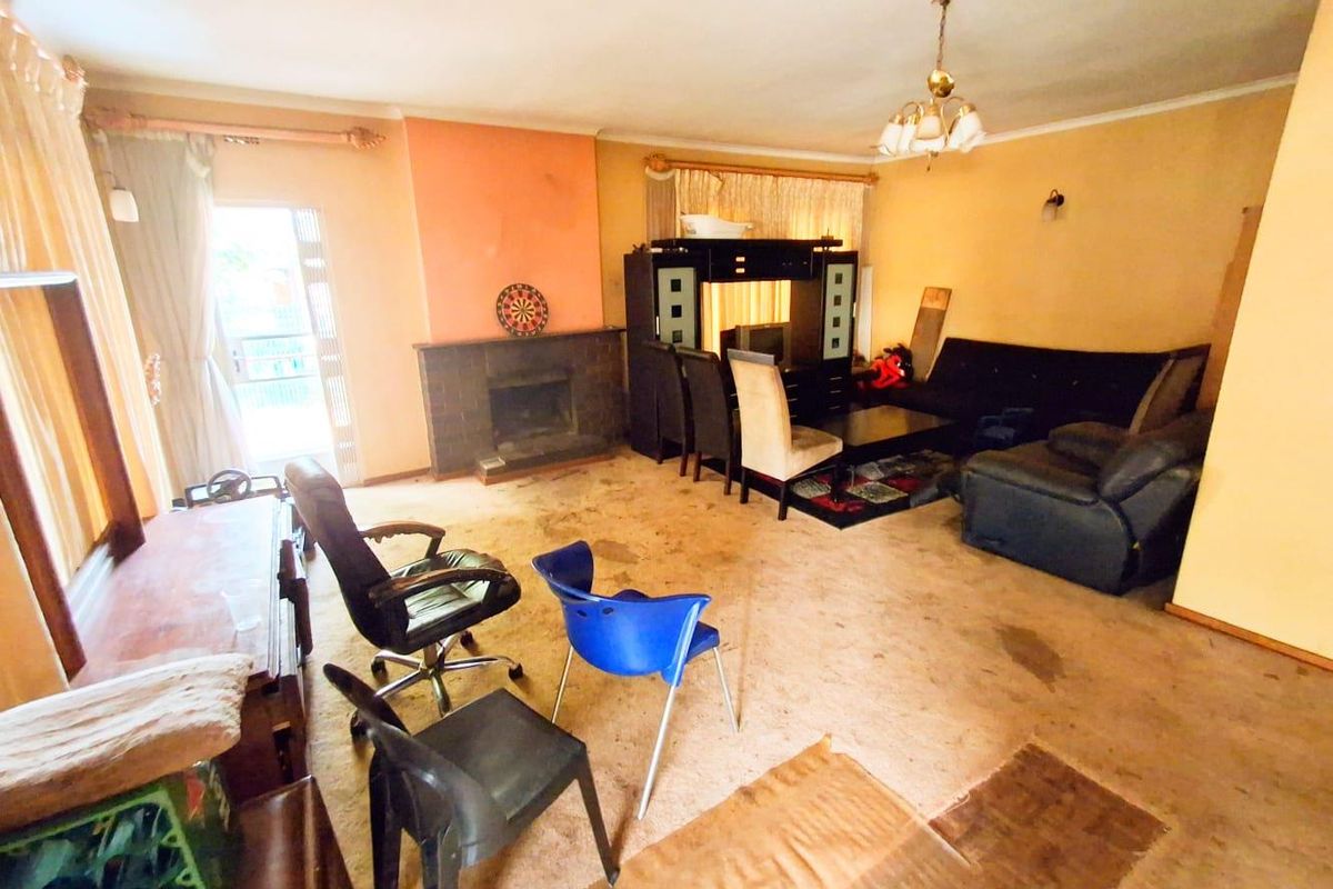 A spacious living room featuring a traditional fireplace, large windows, and carpeted flooring, offering a blank canvas for renovation and modernization.