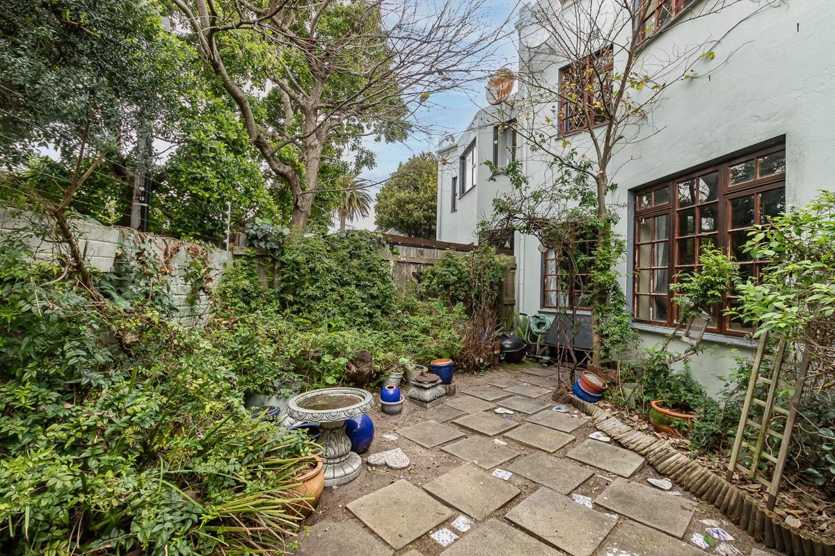 A private rear courtyard featuring paved flooring, established garden beds, and direct access to the townhouse through timber-framed windows.