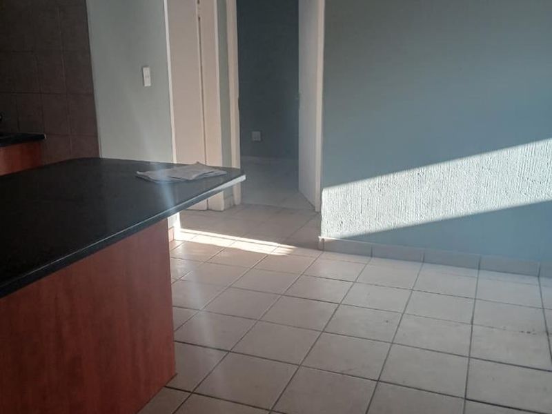 An empty kitchen area featuring a breakfast bar island, tiled flooring, and neutral wall tones, offering a functional space ready for personalization.