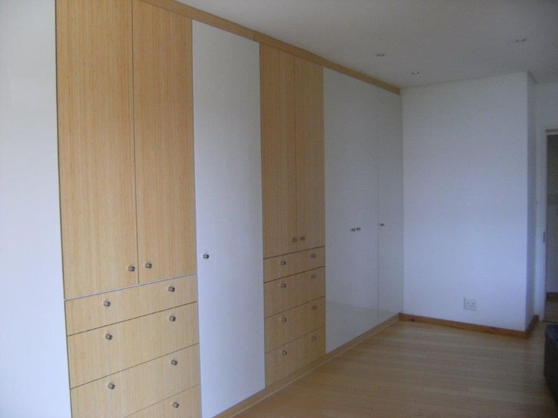 A spacious bedroom featuring extensive floor-to-ceiling built-in cupboards with a modern wood and white finish, complemented by laminate flooring.