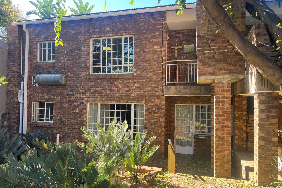 Rear view of a double-story face brick house featuring steel-framed windows, an external geyser, and a paved patio area with balcony access.