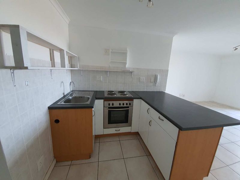 Compact kitchen featuring built-in oven, electric hob, stainless steel sink, and tiled backsplash with ample counter space.