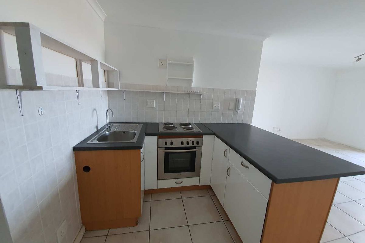 Compact kitchen featuring built-in oven, electric hob, stainless steel sink, and tiled backsplash with ample counter space.