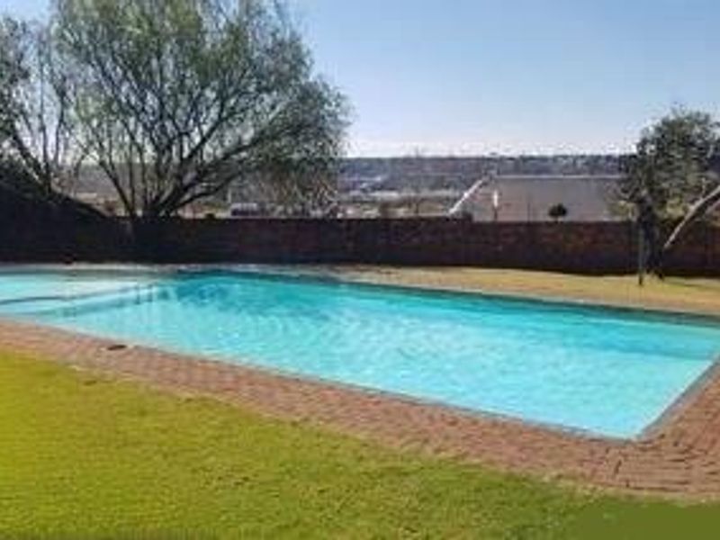 A private swimming pool area featuring a brick-paved surround and a perimeter boundary wall, set within a landscaped garden.