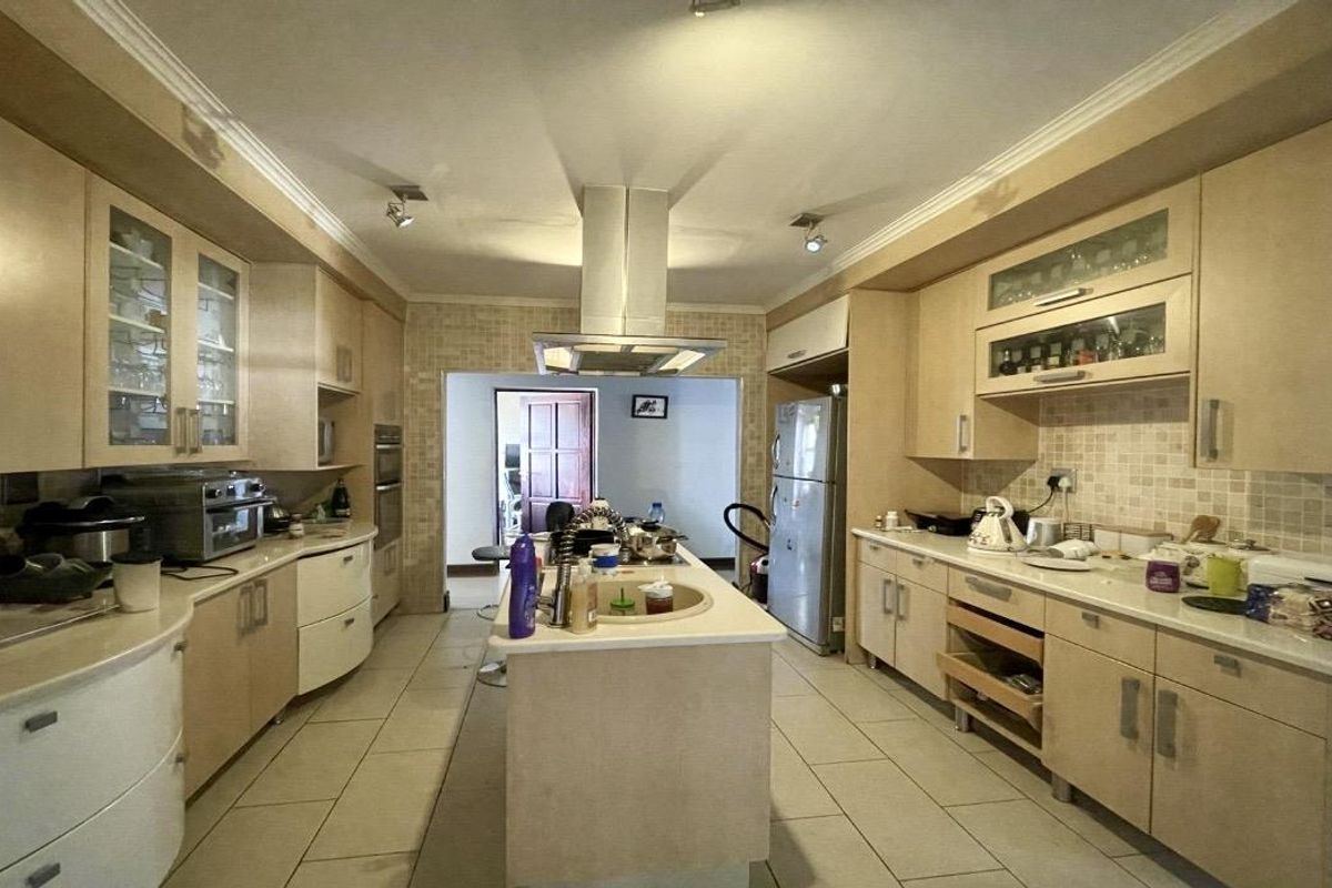 Spacious kitchen featuring a central island, stainless steel extractor fan, built-in oven, and ample cabinetry with a mosaic tile backsplash.