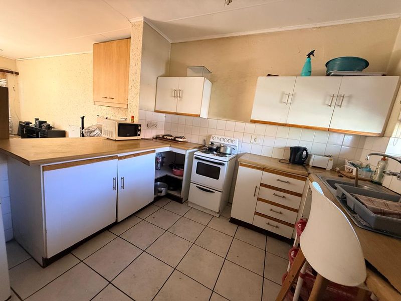 A dated kitchen featuring laminate countertops, tiled backsplash, built-in cabinetry, and a freestanding stove, offering potential for a modern renovation.