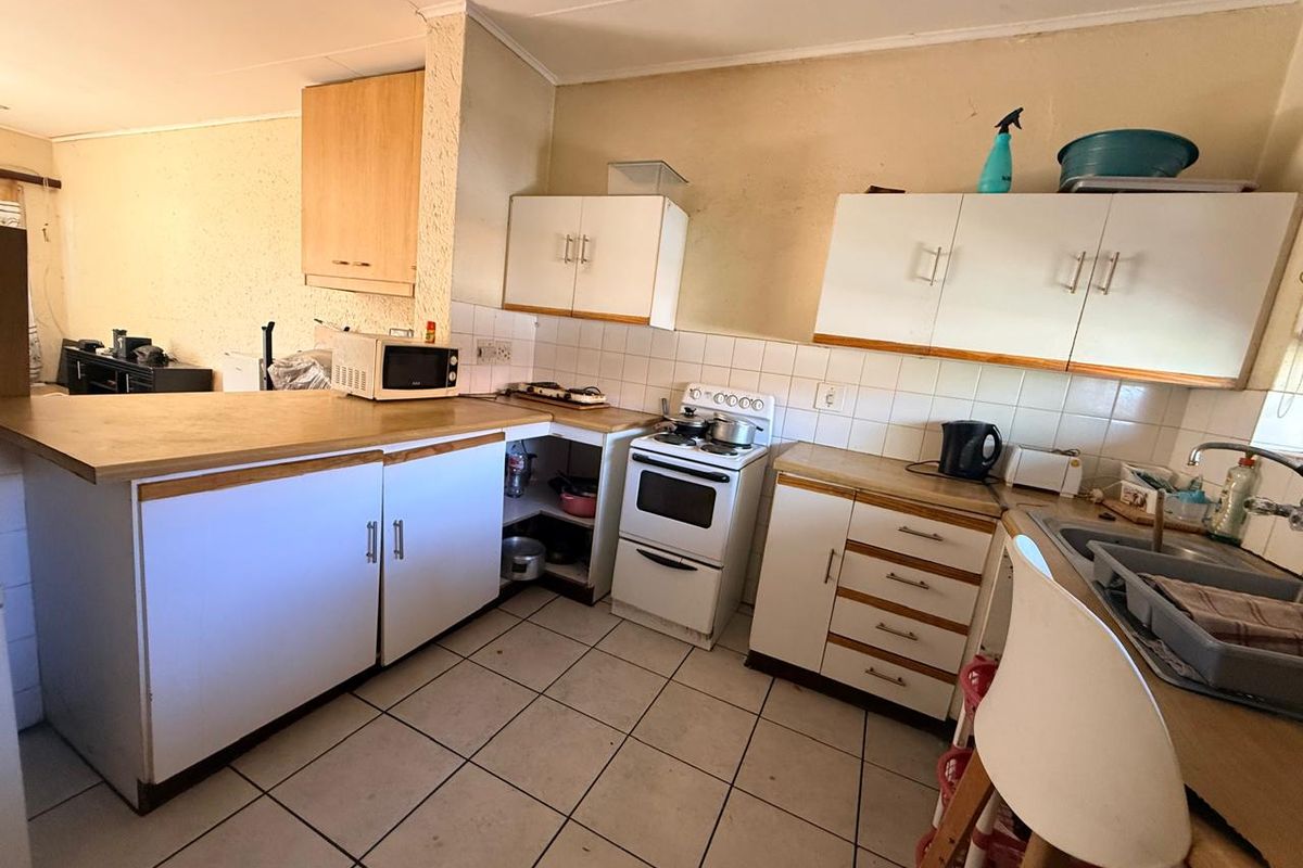 A dated kitchen featuring laminate countertops, tiled backsplash, built-in cabinetry, and a freestanding stove, offering potential for a modern renovation.