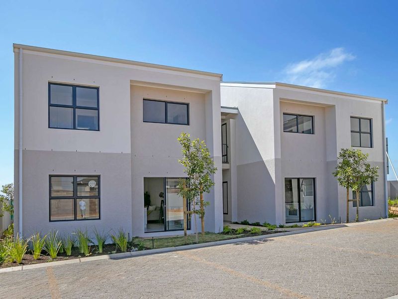 Modern two-story apartment building exterior featuring a paved driveway, clean rendered facade, and large aluminium-framed windows.