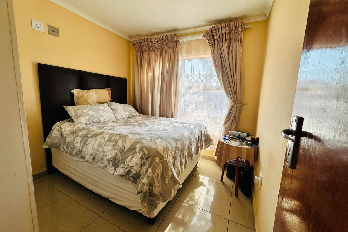 A compact bedroom featuring tiled flooring, a window with security bars, and neutral wall tones, offering a functional space for rest.