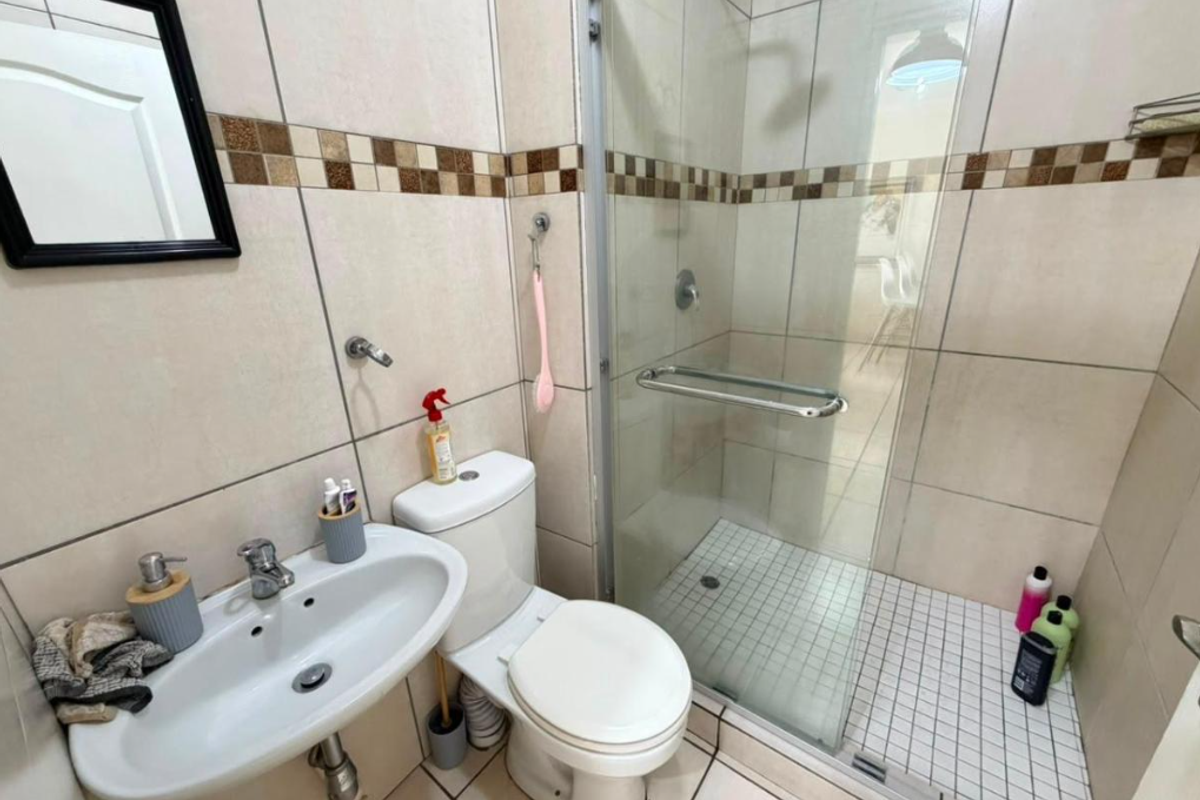 A functional bathroom featuring a pedestal basin, toilet, and a glass-enclosed shower with tiled walls and flooring.