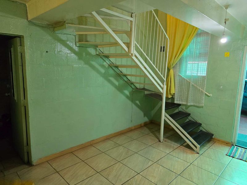 Interior hallway featuring a metal staircase, tiled flooring, and painted concrete block walls, offering a functional space with potential for cosmetic updates.