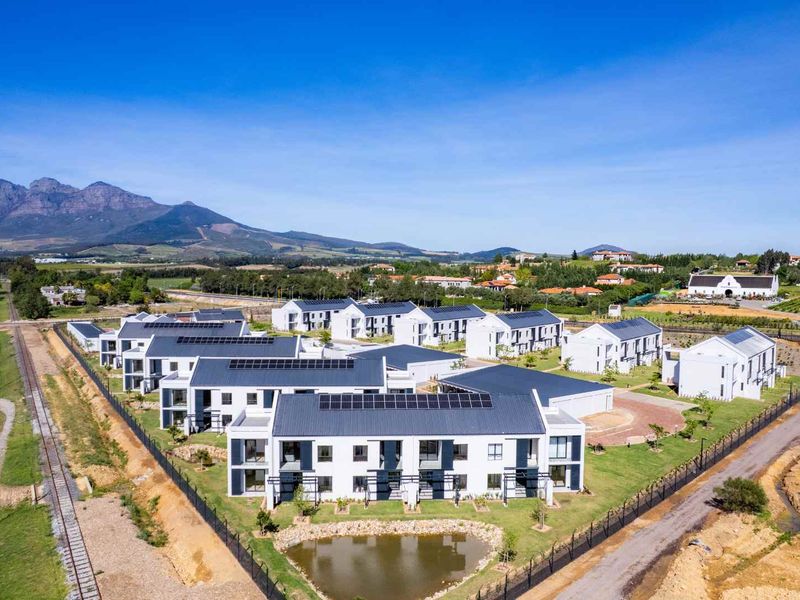 Aerial view of a modern residential apartment complex featuring solar panels, landscaped grounds, and a small pond in a scenic mountain setting.