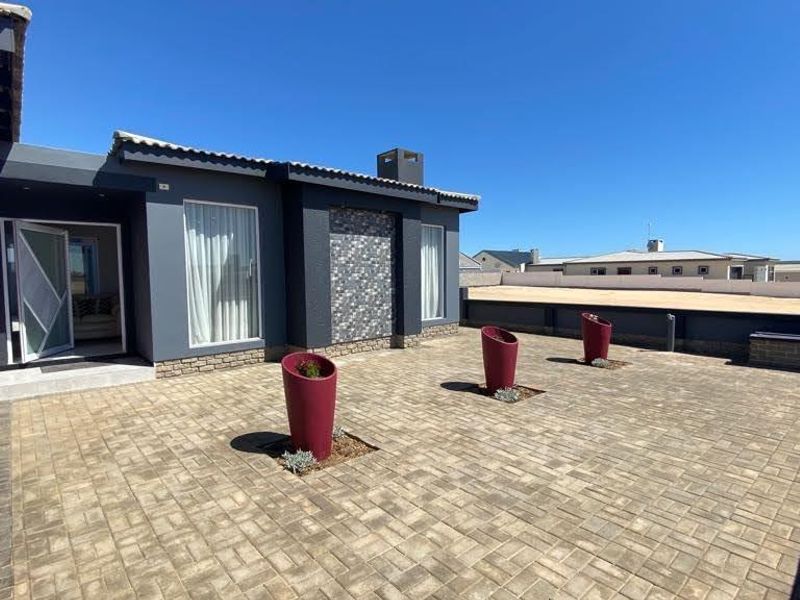 A spacious paved patio area featuring stone-clad wall accents, a chimney, and direct access to the home's interior.