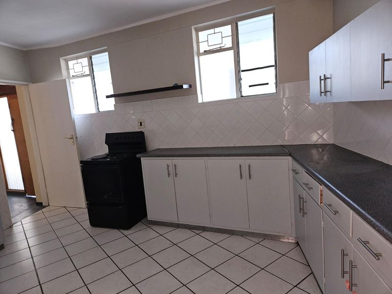 A functional kitchen featuring white cabinetry, dark laminate countertops, a tiled backsplash, and ceramic floor tiles, offering a clean and practical workspace.