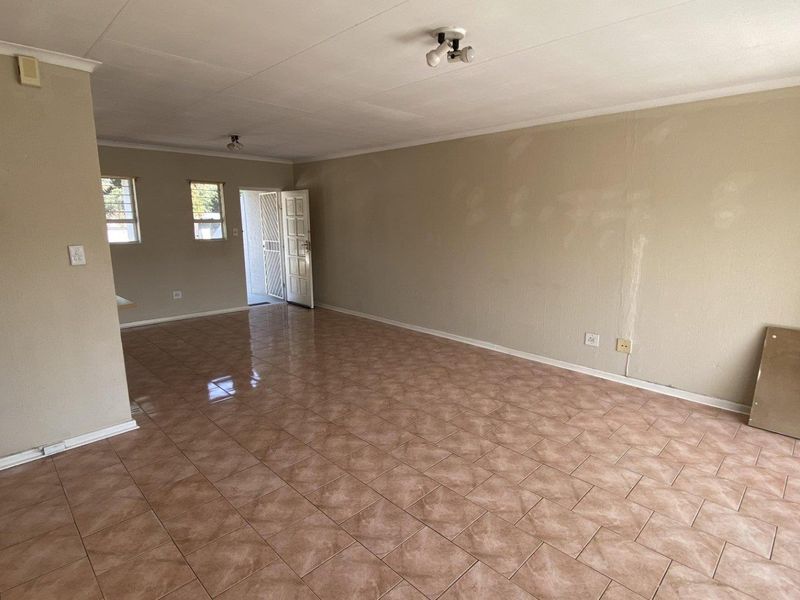 An empty, open-plan living area featuring ceramic floor tiles, neutral walls with visible patching, and access to an outdoor space via a sliding door.