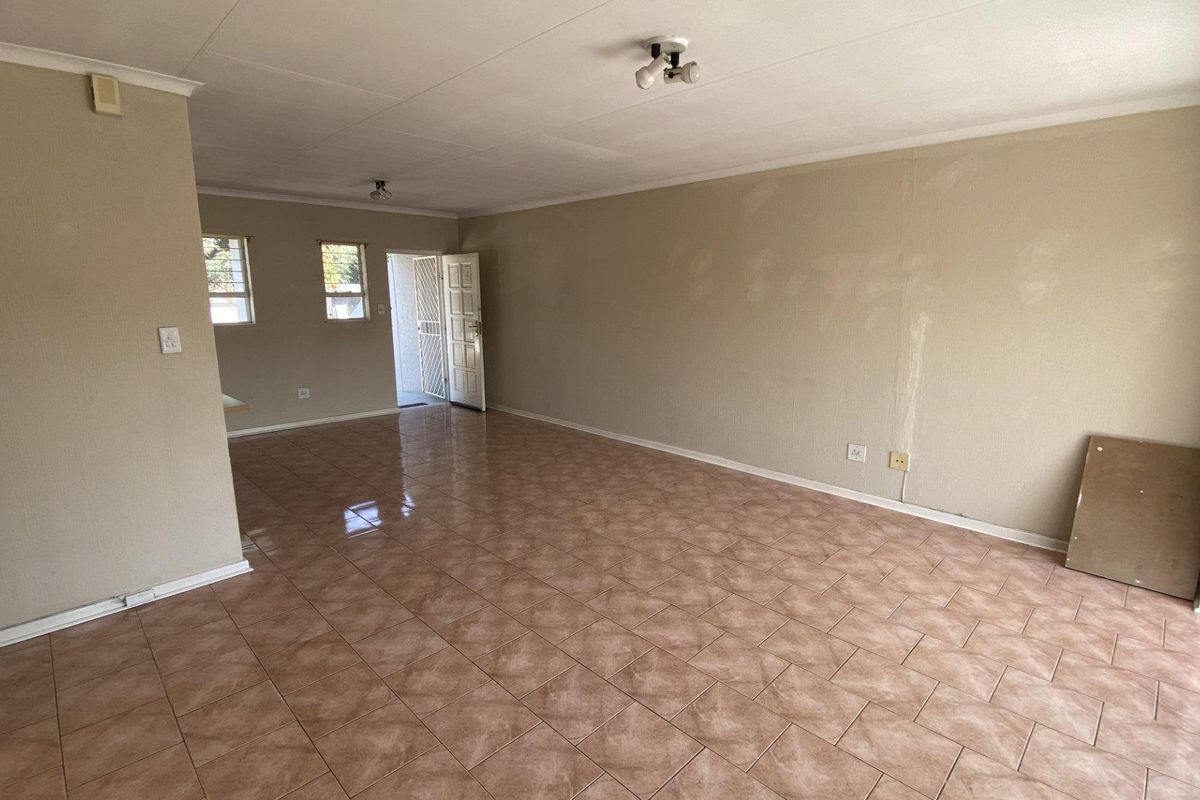 An empty, open-plan living area featuring ceramic floor tiles, neutral walls with visible patching, and access to an outdoor space via a sliding door.