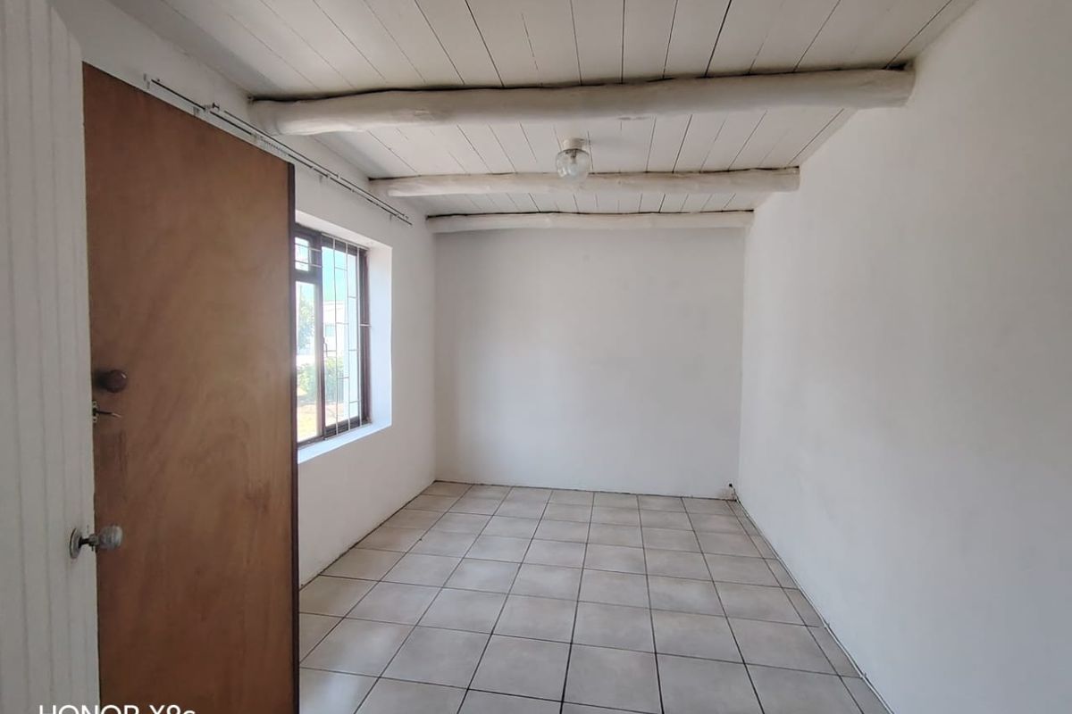 An empty bedroom featuring tiled flooring, a white timber-clad ceiling with exposed beams, and a window fitted with security bars.