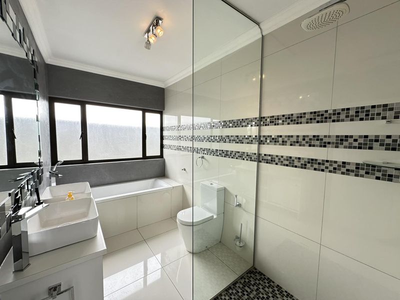 Modern bathroom featuring a double vanity, built-in bathtub, and a spacious glass-enclosed shower with a rain shower head and decorative mosaic tile accents.