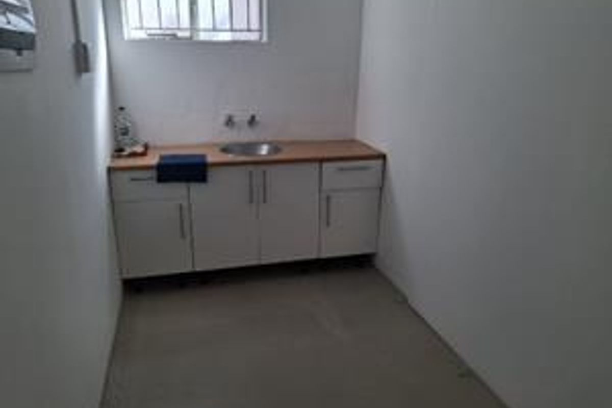 A functional kitchenette area featuring built-in white cabinetry, a stainless steel sink, and a laminate countertop, suitable for office utility use.