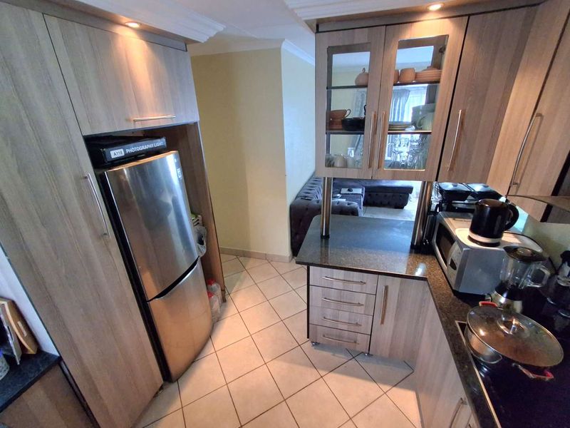 A functional kitchen featuring wood-look cabinetry, granite countertops, glass-fronted display units, and ceramic floor tiles, with a view into the adjacent living area.