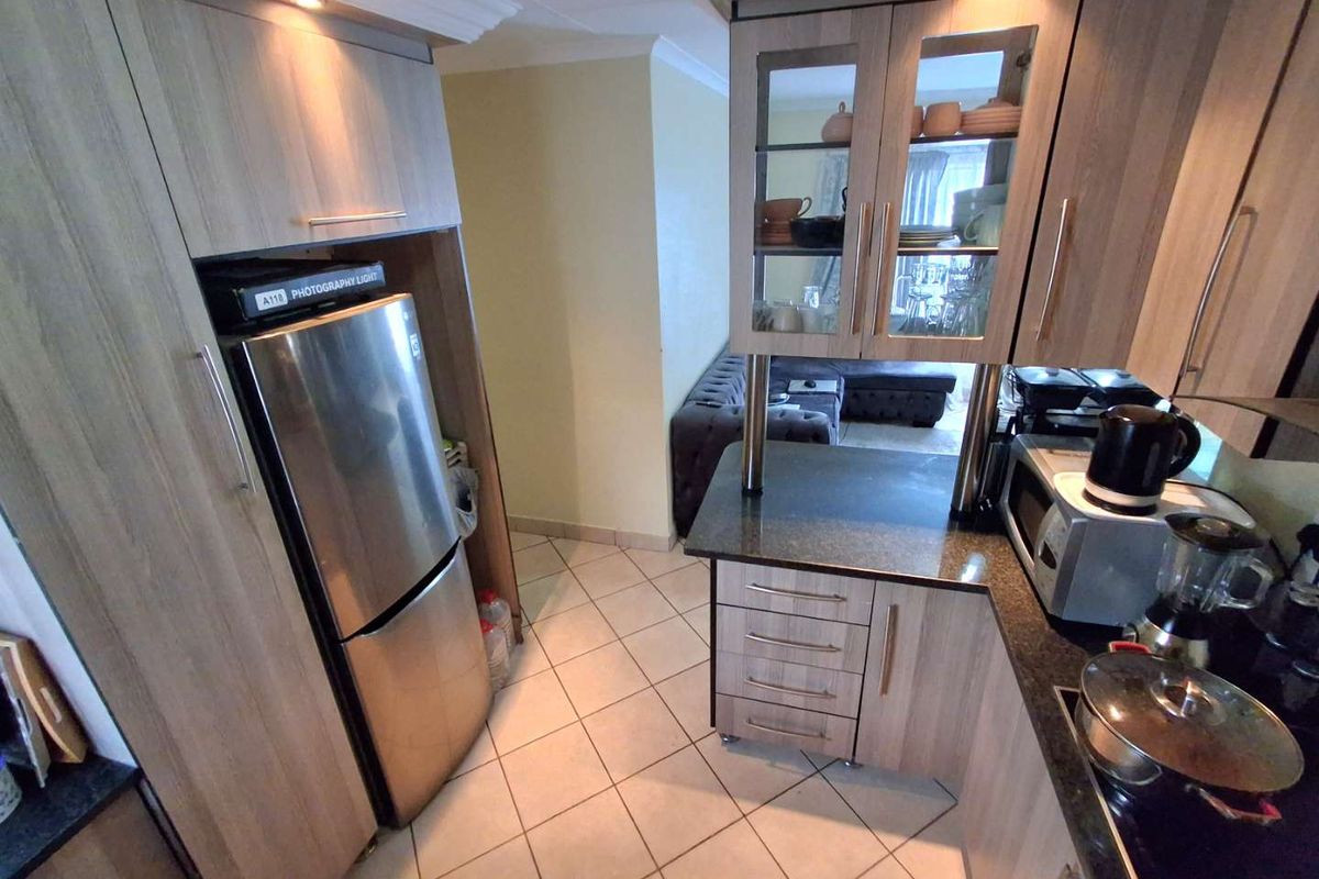 A functional kitchen featuring wood-look cabinetry, granite countertops, glass-fronted display units, and ceramic floor tiles, with a view into the adjacent living area.