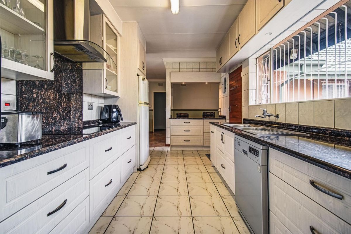 A functional galley-style kitchen featuring granite countertops, ample cabinetry, a stainless steel sink, and integrated extractor fan.