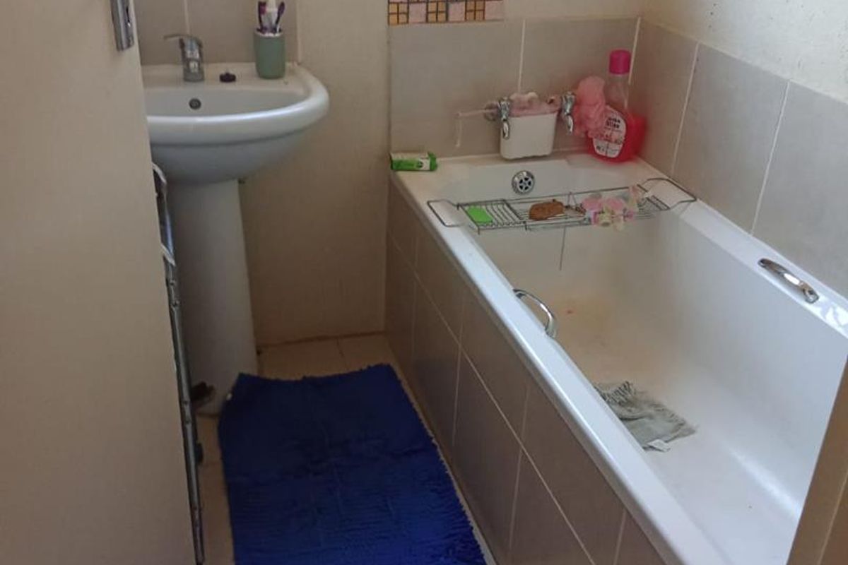 A compact bathroom featuring a standard bathtub with tiled surround, a pedestal basin, and a window with security bars.
