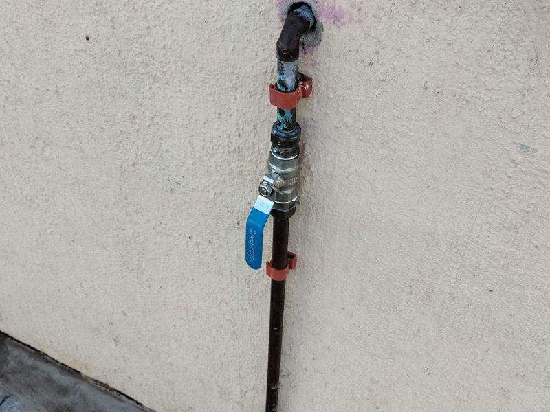 Close-up view of an external water shut-off valve and exposed plumbing pipework mounted on the exterior wall.