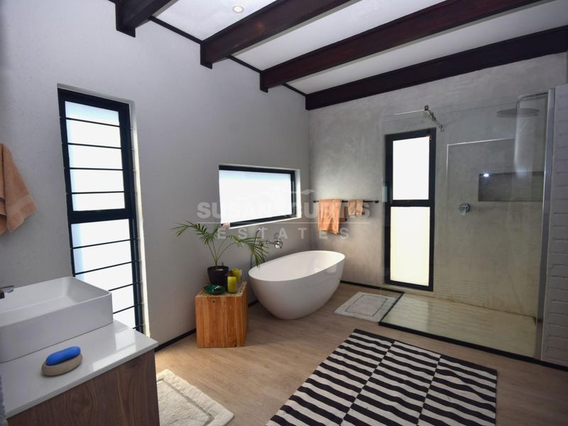 Modern bathroom featuring a freestanding bathtub, walk-in shower with glass enclosure, exposed timber ceiling beams, and a contemporary vanity with a vessel sink.