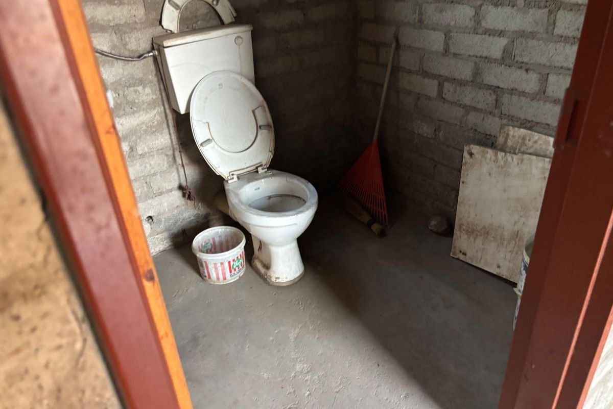 A basic, unfinished bathroom featuring a standard toilet, exposed brick walls, and a concrete floor, requiring significant renovation and finishing work.