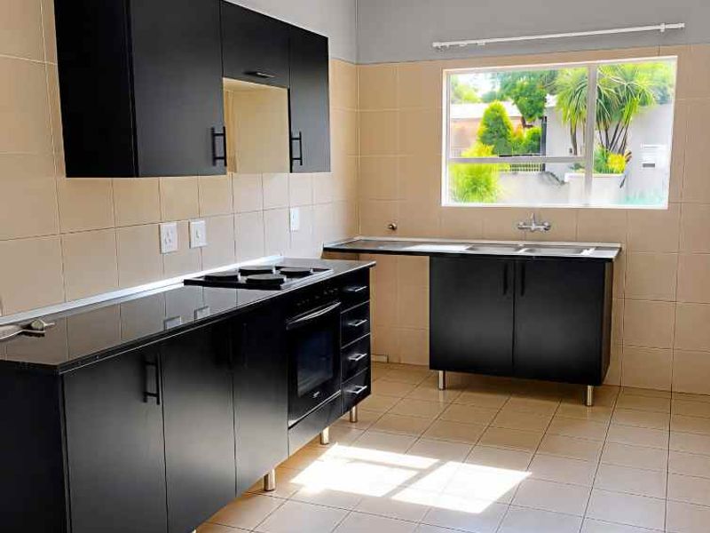 A clean, empty kitchen featuring modern black cabinetry, built-in oven, hob, and a double sink with tiled splashbacks and flooring.
