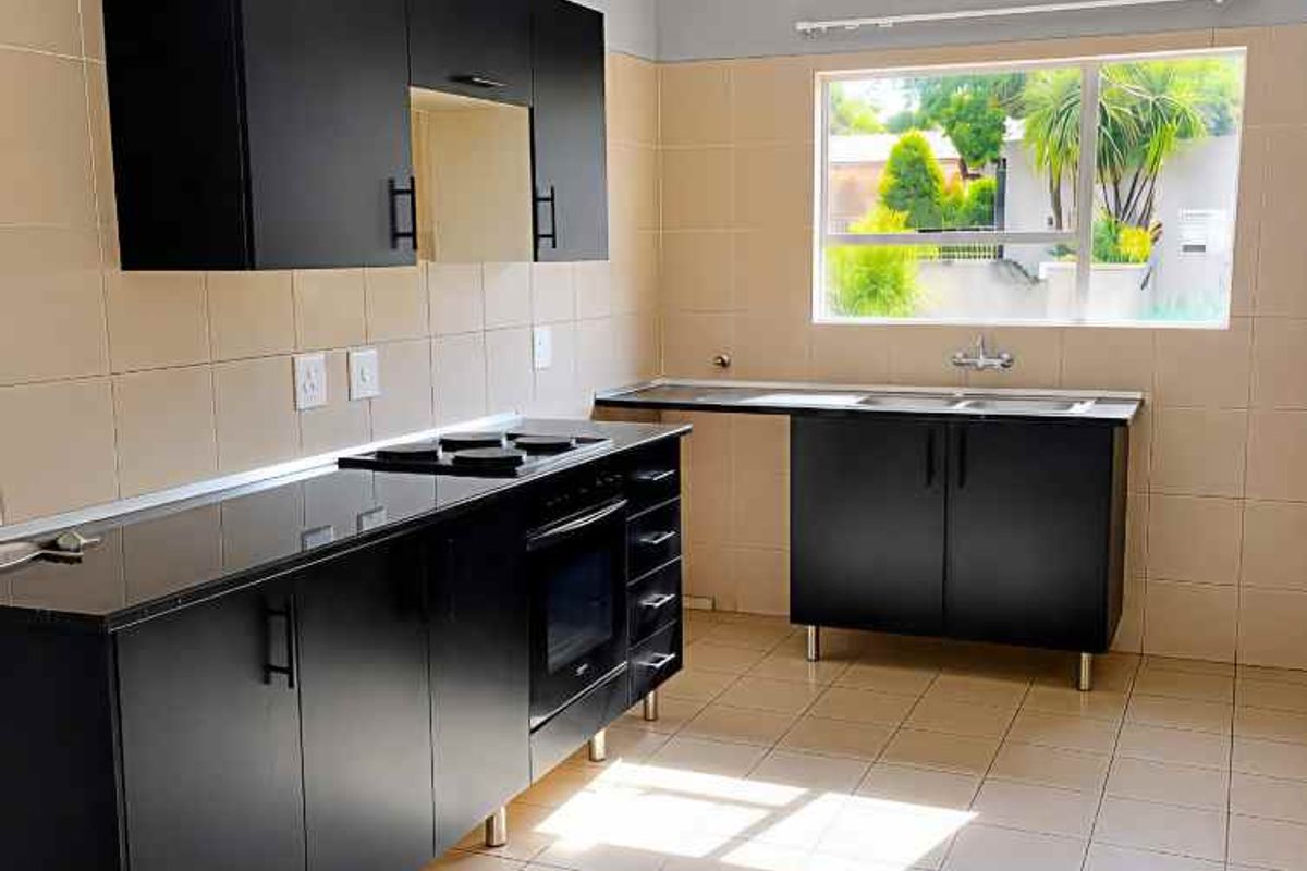 A clean, empty kitchen featuring modern black cabinetry, built-in oven, hob, and a double sink with tiled splashbacks and flooring.