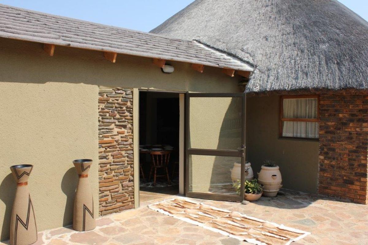 A view of the rear exterior featuring a traditional thatched roof, stone-clad accents, and a paved patio area leading into the home.