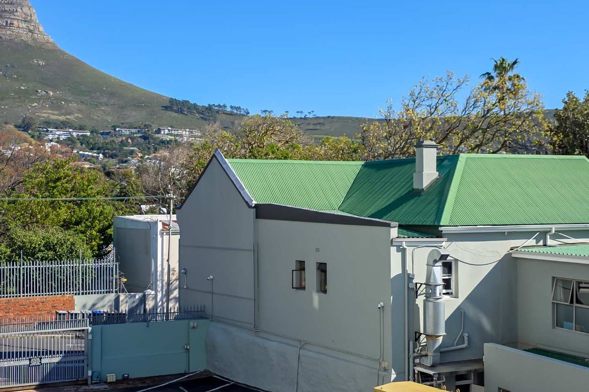 Rear exterior view of the property featuring a green corrugated metal roof, chimney, and paved parking area with mountain views in the background.