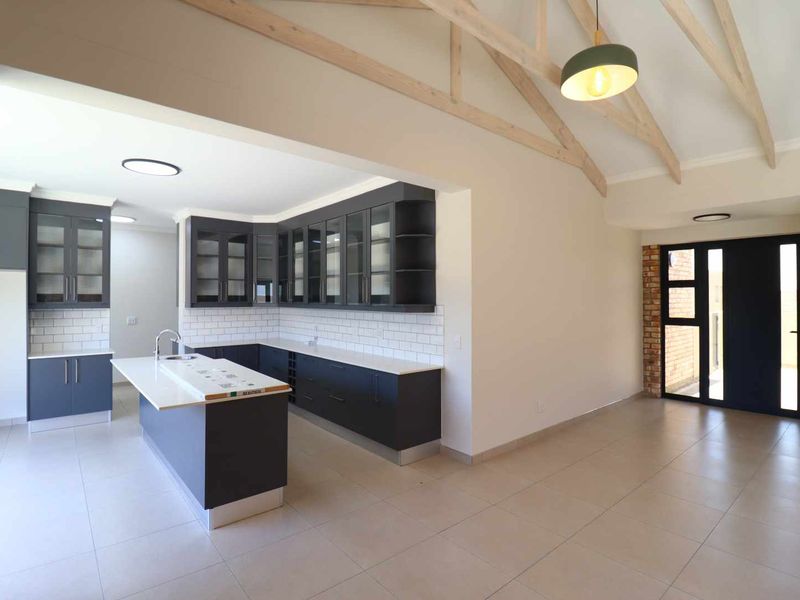 Spacious open-plan kitchen featuring modern dark cabinetry, a central island, subway tile backsplash, and high ceilings with exposed timber trusses.