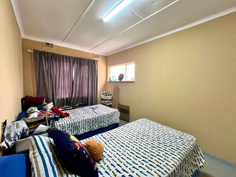 A bedroom featuring a window and ceiling ventilation, currently showing signs of wear including cracked ceiling panels and peeling paint.