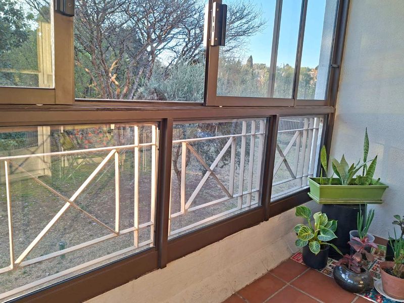 A covered balcony featuring terracotta floor tiles, sliding glass doors, and integrated metal security bars overlooking a garden area.