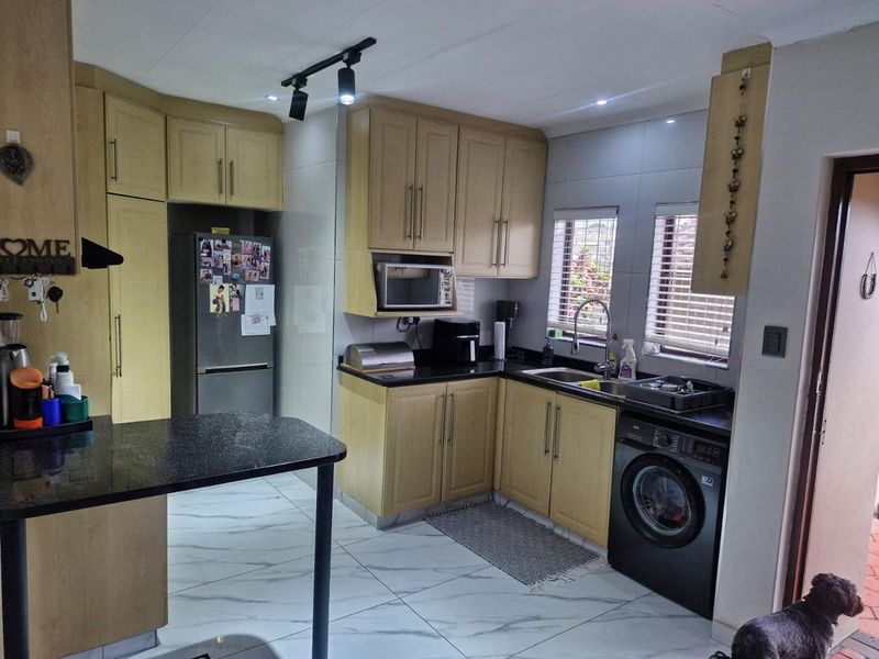 A functional kitchen featuring light wood cabinetry, dark granite countertops, modern tiled flooring, and integrated laundry facilities with track lighting.