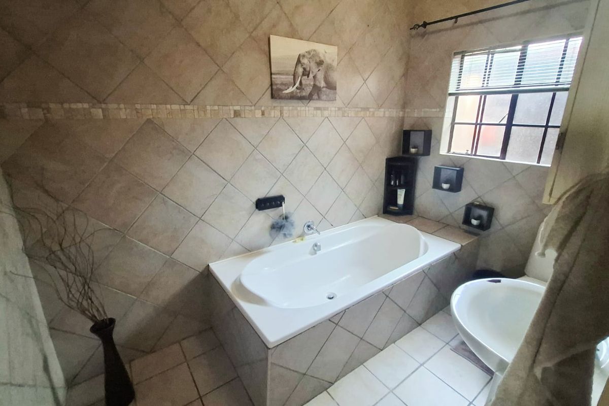 A functional bathroom featuring a built-in bathtub with tiled surround, ceramic wall and floor tiling, and a window with security bars.