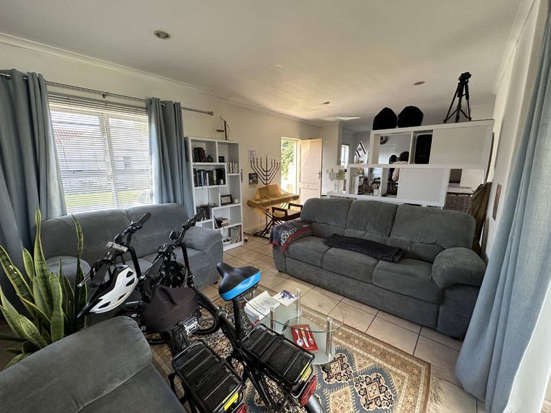 A living room area featuring tiled flooring, recessed downlighting, and large windows with venetian blinds, providing a functional and well-lit space.