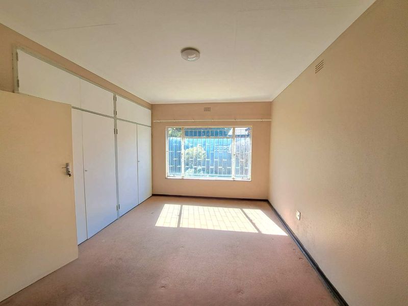 An empty bedroom featuring built-in cupboards, carpet flooring, and a window with security bars.