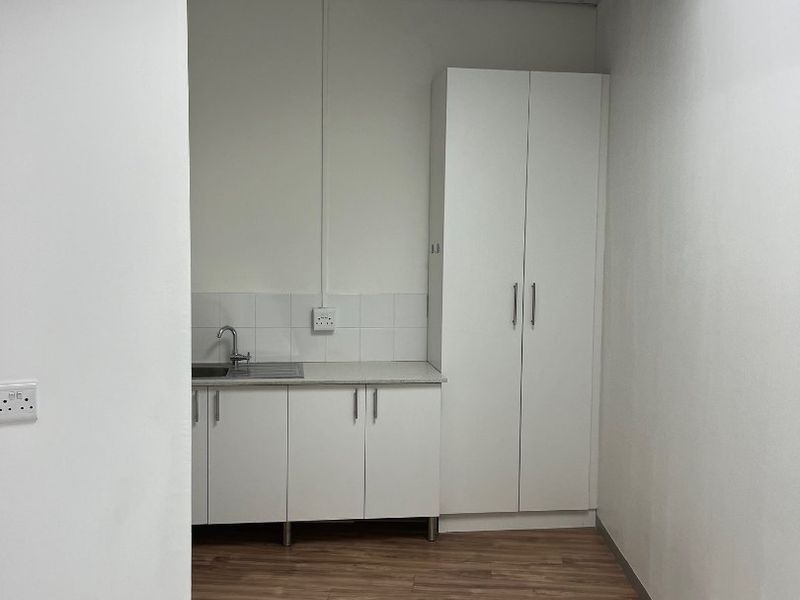 A clean, compact kitchenette area featuring white built-in cabinetry, a stainless steel sink, and wood-look flooring, suitable for office or retail utility use.