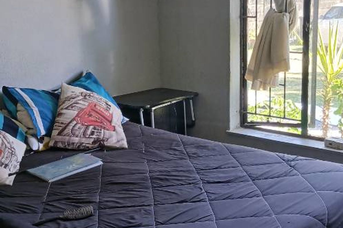 A bedroom featuring tiled flooring and a window with security bars, offering natural light and a view of the exterior.