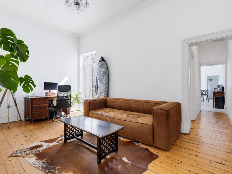 A bright living room featuring original timber flooring, high ceilings with beadboard detailing, and classic architectural trim throughout.
