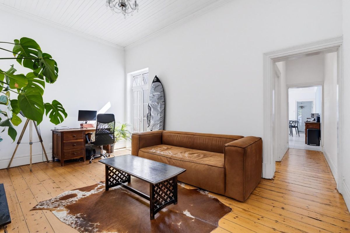 A bright living room featuring original timber flooring, high ceilings with beadboard detailing, and classic architectural trim throughout.