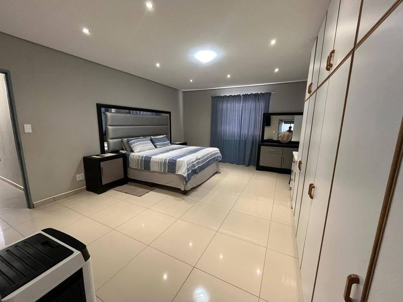 Spacious bedroom featuring neutral tiled flooring, recessed downlighting, and extensive built-in cupboard storage.